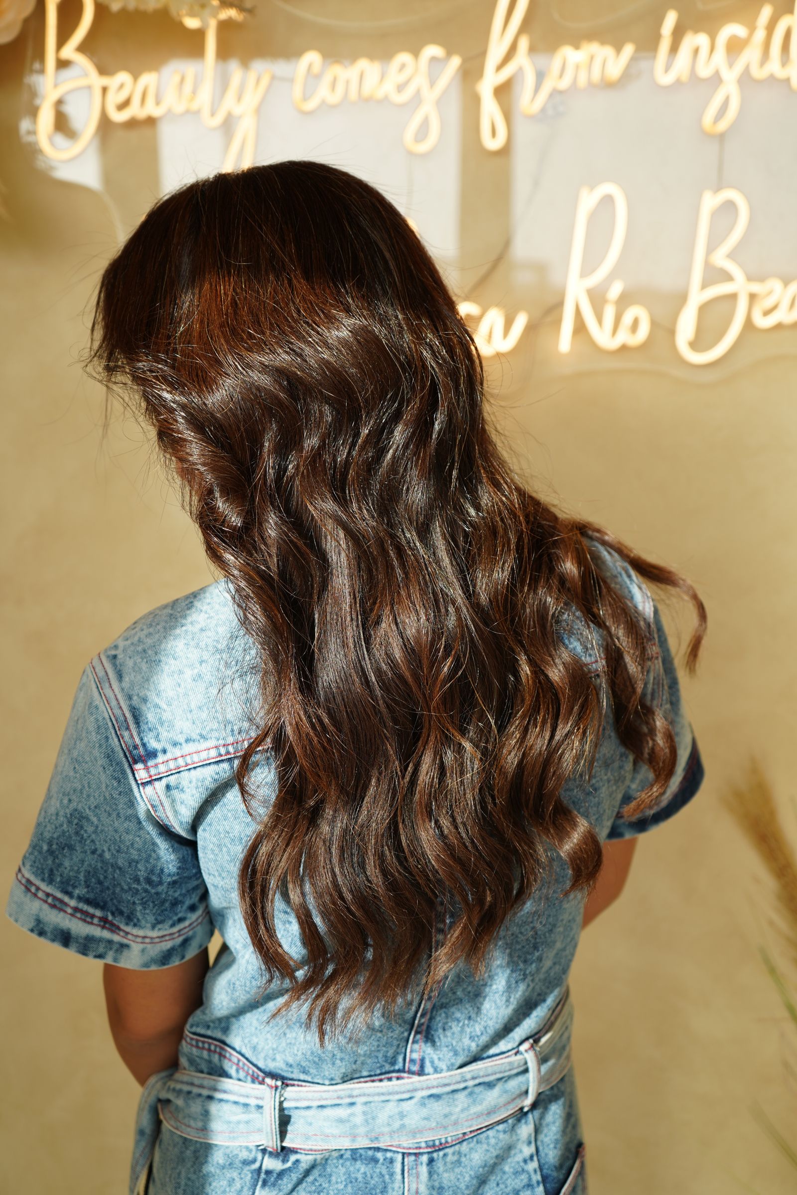 Close-up of woman with wavy brown hair in modern salon with neon sign.