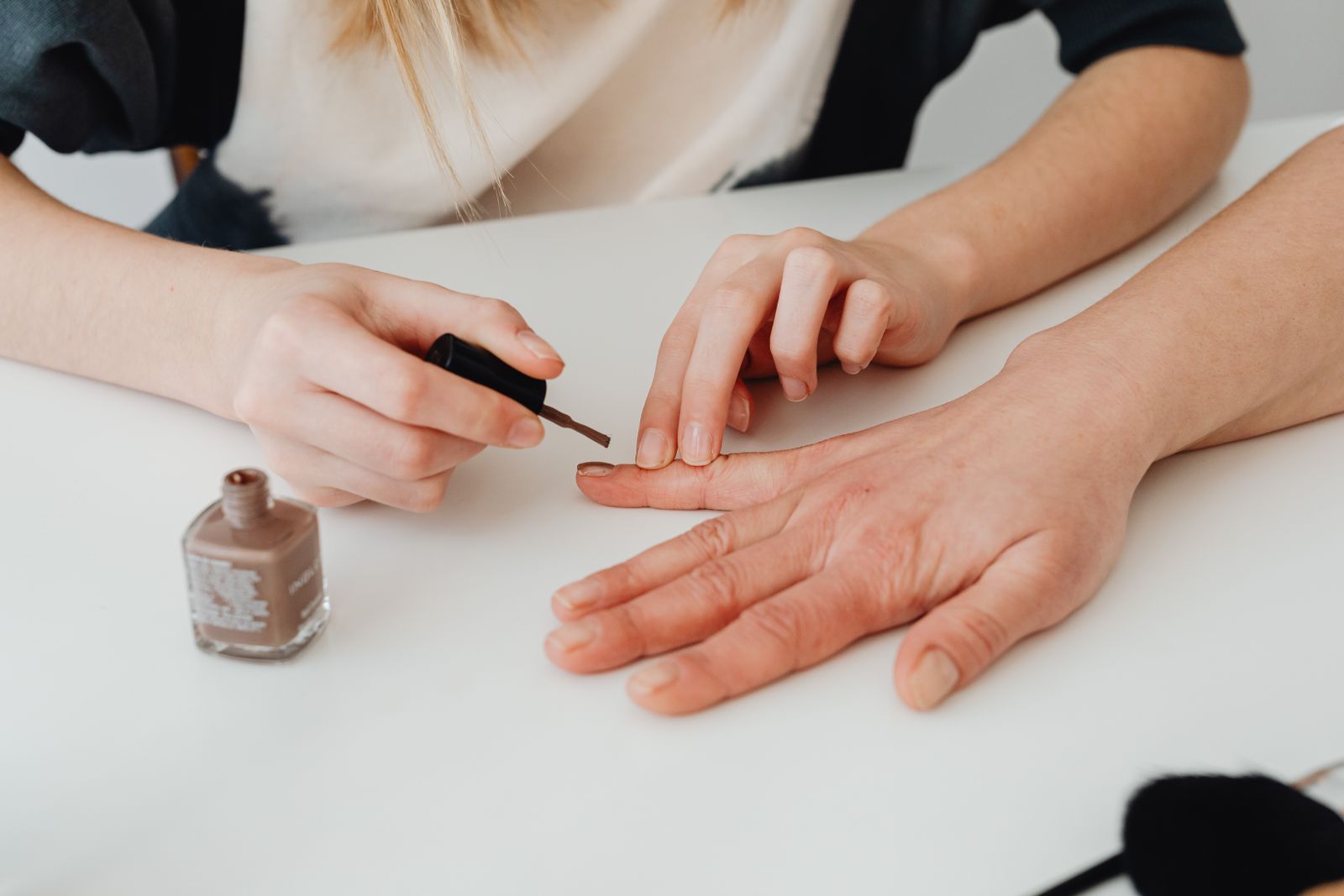 A nail technician painting a nude polish