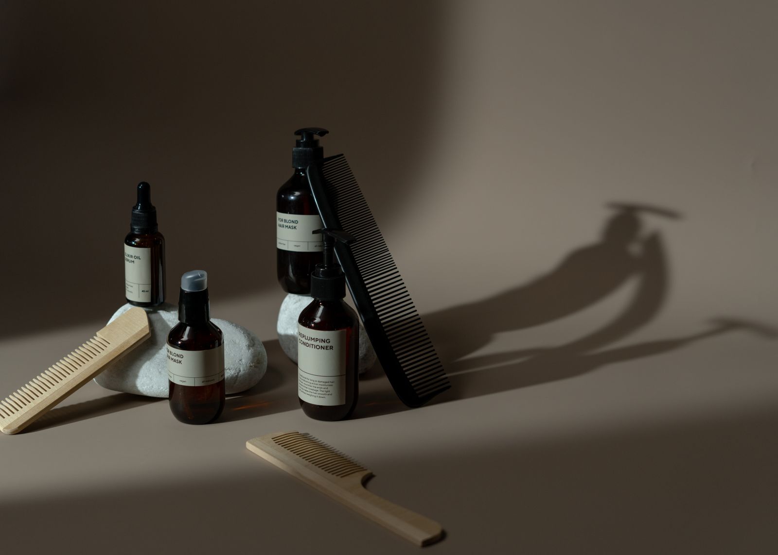 Amber hair care bottles and a wide-tooth comb on a stone surface
